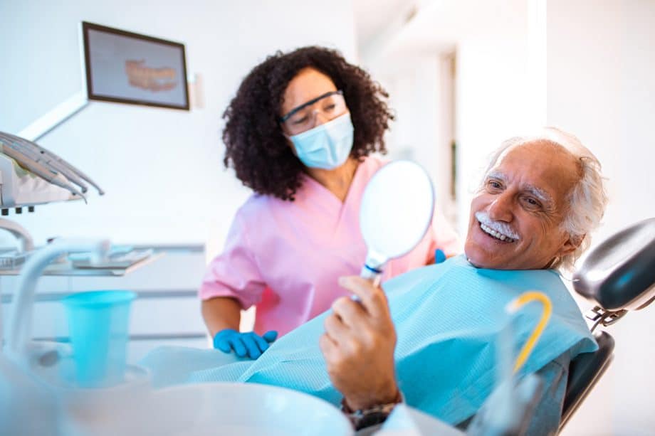 male patient looking in mirror smiling while dental hygienist looks on